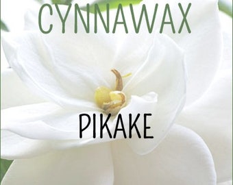 以下が含まれることがあります： 「CYNNAWAX PIKAKE SOY & BEESWAX MELTS」の文字が緑と黒で書かれた白い花のクローズアップ。花は白い花びらが何層にもなっており、中心は黄色です。