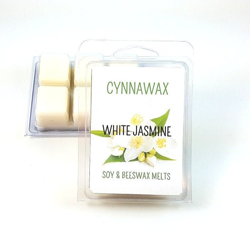 Puede incluir: Un paquete de cera de soja y cera de abeja blanca con una etiqueta que dice "Cynnawax White Jasmine Soy & Beeswax Melts". La etiqueta presenta una flor de jazm&iacute;n blanca.