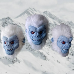May include: Three white yeti masks with blue faces and red eyes. The masks have a furry white texture and are looking forward with a fierce expression.