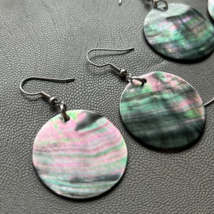 May include: A pair of earrings with silver hooks and round, iridescent, black, green, and pink shell pendants.