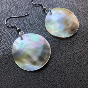 May include: A pair of silver earrings with iridescent round shell pendants. The shells have a pearlescent finish with shades of green, blue, and brown.
