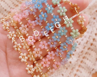Puede incluir: Un conjunto de ocho pulseras de cuentas con cuentas con forma de flor en varios colores pastel, incluyendo azul claro, rosa, amarillo y verde. Las pulseras están etiquetadas de la A a la H.