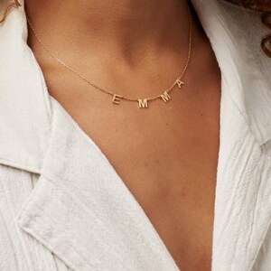 May include: A gold chain necklace with the name "EMMA" spelled out in small, hanging letters.