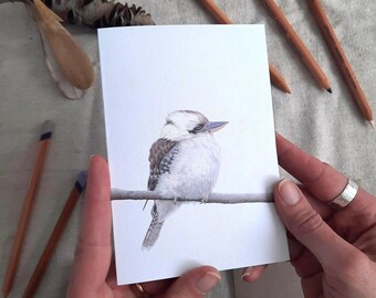 以下が含まれることがあります： 枝に止まっているオニオオハシの水彩画。鳥は灰色と白のグラデーションで描かれており、青い嘴と目をしています。