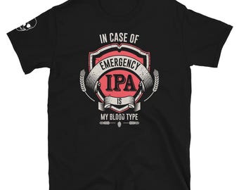May include: Black t-shirt with a graphic design that reads "IN CASE OF EMERGENCY IPA IS MY BLOOD TYPE" in white and red lettering. The design includes a shield, banner, and wheat stalks. A small skull graphic is on the left sleeve.