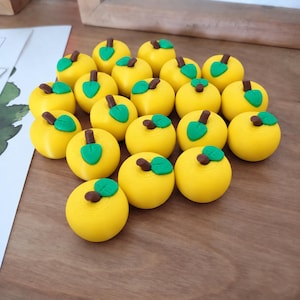 May include: A collection of twenty small, round, yellow apple-shaped figures. Each apple features a brown stem and a single green leaf attached to the top. The figures are arranged in a cluster, displaying a smooth, uniform surface texture throughout.