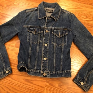 May include: A blue denim jacket with a button closure and two front pockets. The jacket has a label that reads "Sonnez" on the inside of the collar.
