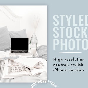 May include: A laptop computer with a blank screen is open on a white bed with gray bedding. A glass vase with dried white flowers and a glass of milk are on a tray next to the laptop. An open book is on the bed in front of the laptop.