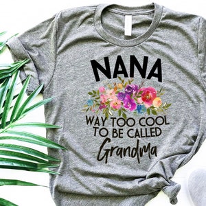 Puede incluir: Camiseta gris con un dise&ntilde;o floral y el texto "NANA WAY TOO COOL TO BE CALLED GRANDMA".