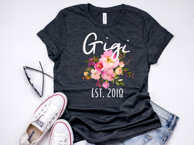 May include: A dark gray t-shirt with the text "Gigi Est. 2018" and a floral design in pink, yellow, and green.