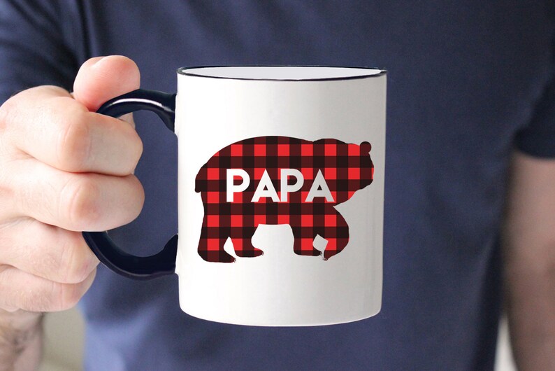 Puede incluir: Taza de cer&aacute;mica blanca con asa y borde negros. La taza presenta una silueta de oso en patr&oacute;n de cuadros rojos y negros con la palabra "PAPA" en letras blancas.