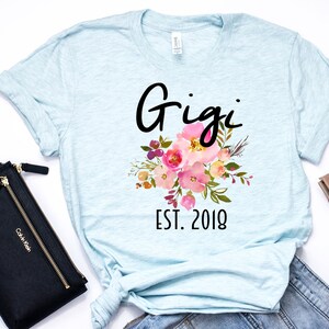 May include: Light blue t-shirt with a floral design and the text "Gigi Est. 2018".