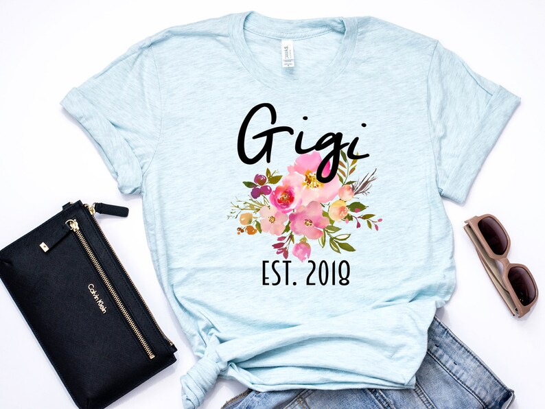 May include: Light blue t-shirt with a floral design and the text "Gigi Est. 2018".