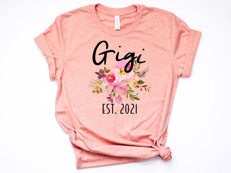 May include: A peach-colored t-shirt with the text "Gigi Est. 2021" and a floral design in pink, yellow, and green.