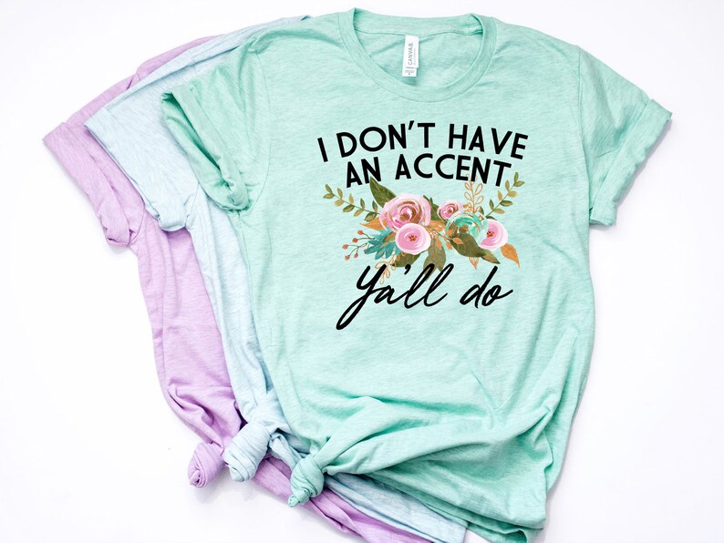 以下が含まれることがあります： 花柄のライトグリーンのTシャツに、黒い文字で「I don't have an accent y'all do」と書いてあります。