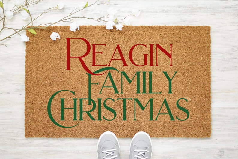 Puede incluir: Una alfombra de coco marr&oacute;n con el texto "Reagin Family Christmas" en letras rojas y verdes.