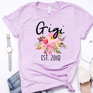 May include: A lavender t-shirt with a floral design and the text "Gigi Est. 2018".