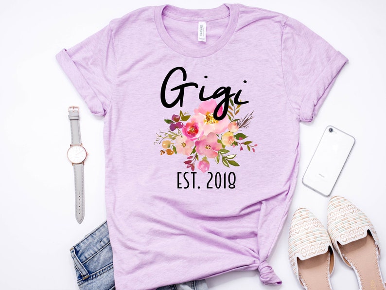 May include: A lavender t-shirt with a floral design and the text "Gigi Est. 2018".