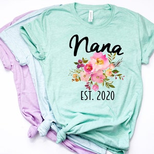 Puede incluir: Una camiseta verde claro con un dise&ntilde;o floral y el texto "Nana Est. 2020".