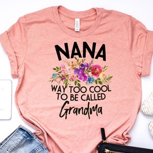 Puede incluir: Una camiseta rosa con un dise&ntilde;o floral y el texto "NANA WAY TOO COOL TO BE CALLED GRANDMA".
