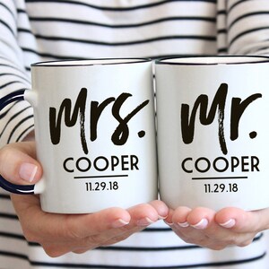 May include: Two white ceramic mugs with black handles and black lettering. The mugs say "Mrs. Cooper 11.29.18" and "Mr. Cooper 11.29.18".