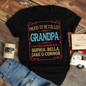 May include: Black t-shirt with a vintage-style sign that says "Proud to be called Grandpa" with the names "Sophia, Bella, Jake & Connor" underneath.