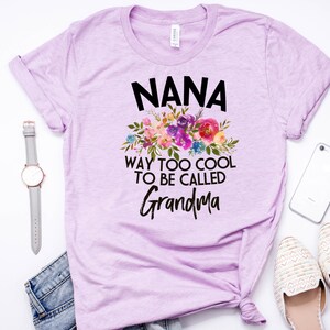 Puede incluir: Una camiseta lavanda con un dise&ntilde;o floral y el texto "NANA WAY TOO COOL TO BE CALLED GRANDMA".