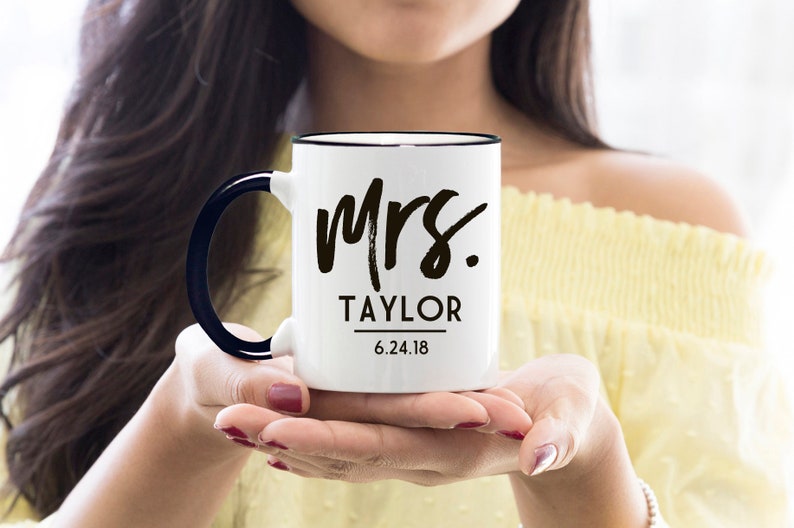 May include: White ceramic mug with a black rim and handle. The mug has black text that reads "Mrs. Taylor 6.24.18".