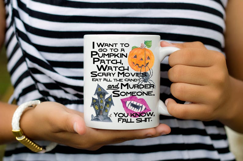 May include: White ceramic mug with a black and white illustration of a haunted house, a pumpkin, a spider, and a set of lips with fangs. The text on the mug reads "I want to go to a pumpkin patch, watch scary movies, eat all the candy and murder someone. You know, fall shit."