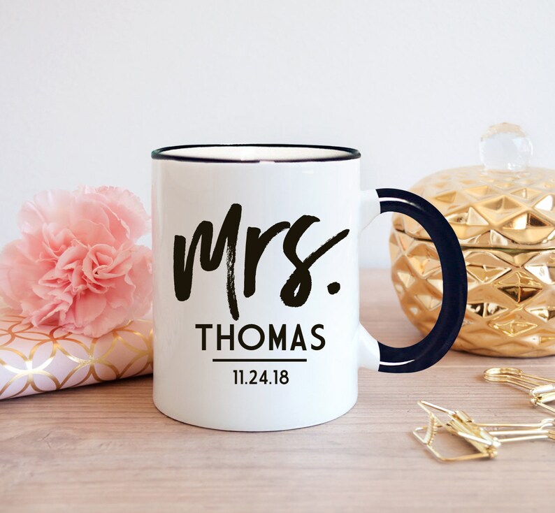 May include: White ceramic mug with a black rim and handle. The mug has black text that says "Mrs. THOMAS 11.24.18".