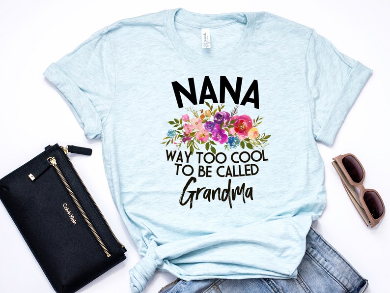 Puede incluir: Camiseta azul claro con un dise&ntilde;o floral y el texto "NANA WAY TOO COOL TO BE CALLED GRANDMA".