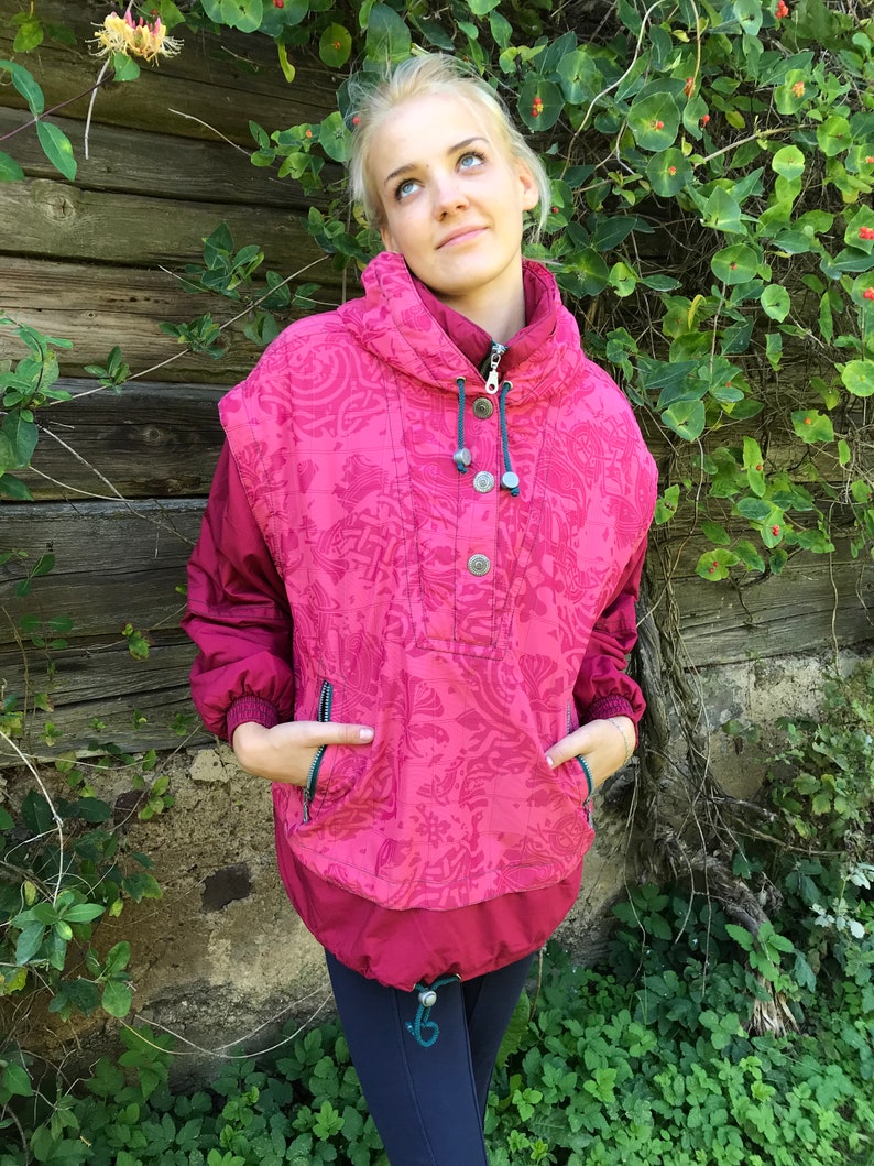 May include: A pink and red patterned jacket with a high collar and a snap closure. The jacket has a drawstring hood and two pockets.