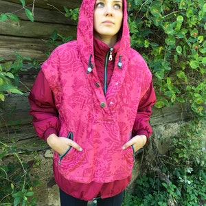 May include: A pink hooded jacket with a patterned design and a zipper closure. The jacket has two pockets on the front and a drawstring at the bottom.