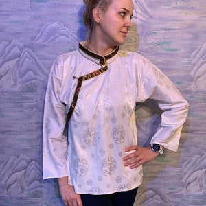 May include: A white long-sleeved shirt with a mandarin collar and a gold and brown trim. The shirt has a pattern of silver circles with a floral design.