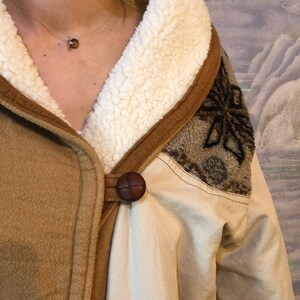 May include: A brown suede jacket with a white sherpa lining and a brown button closure. The jacket has a patterned design on the back.