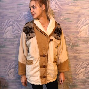 May include: A beige and brown patchwork jacket with a sherpa collar and brown buttons. The jacket has a geometric pattern on the shoulders and a brown suede trim.
