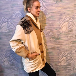 May include: A cream-colored jacket with a brown corduroy collar and brown corduroy sleeves. The jacket has a snowflake design on the left shoulder and a brown button closure.