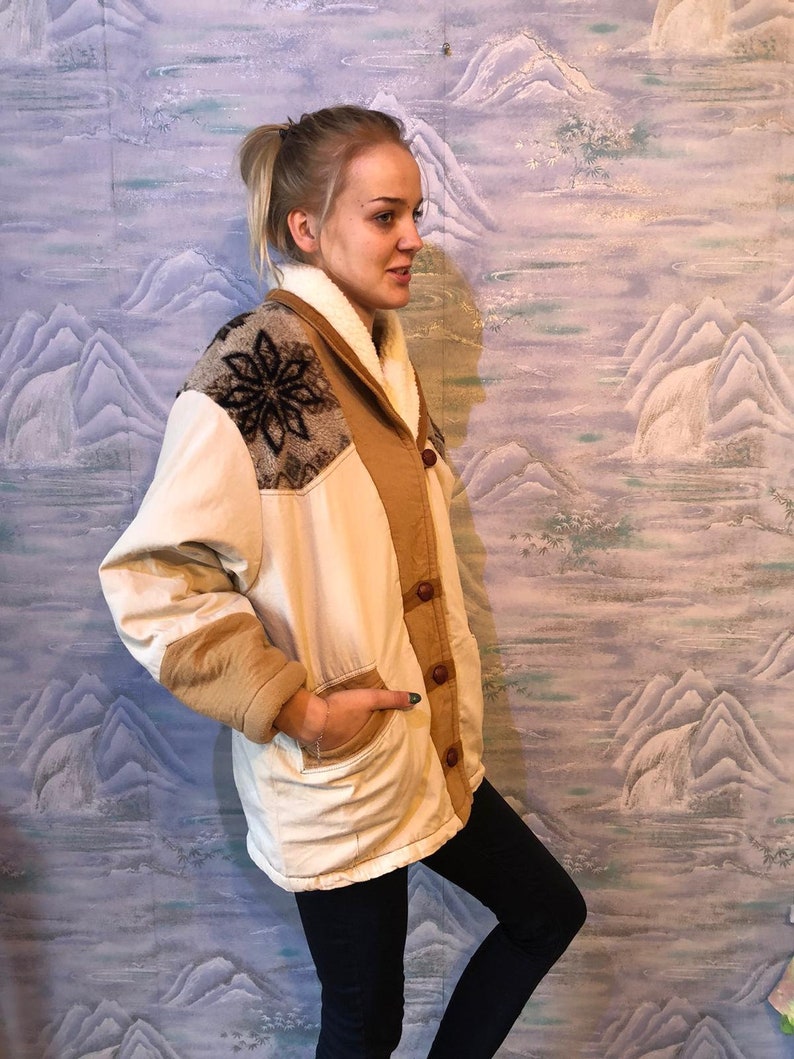 May include: A cream-colored jacket with a brown corduroy collar and brown corduroy sleeves. The jacket has a snowflake design on the left shoulder and a brown button closure.