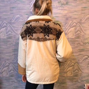 May include: A cream-colored jacket with a brown faux fur collar and a brown and white geometric pattern on the back. The jacket has a zipper closure and long sleeves.