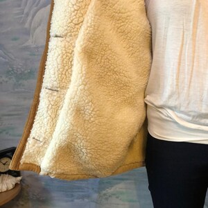 May include: A brown suede jacket with a cream-colored sherpa lining. The jacket has a button closure and a collar.