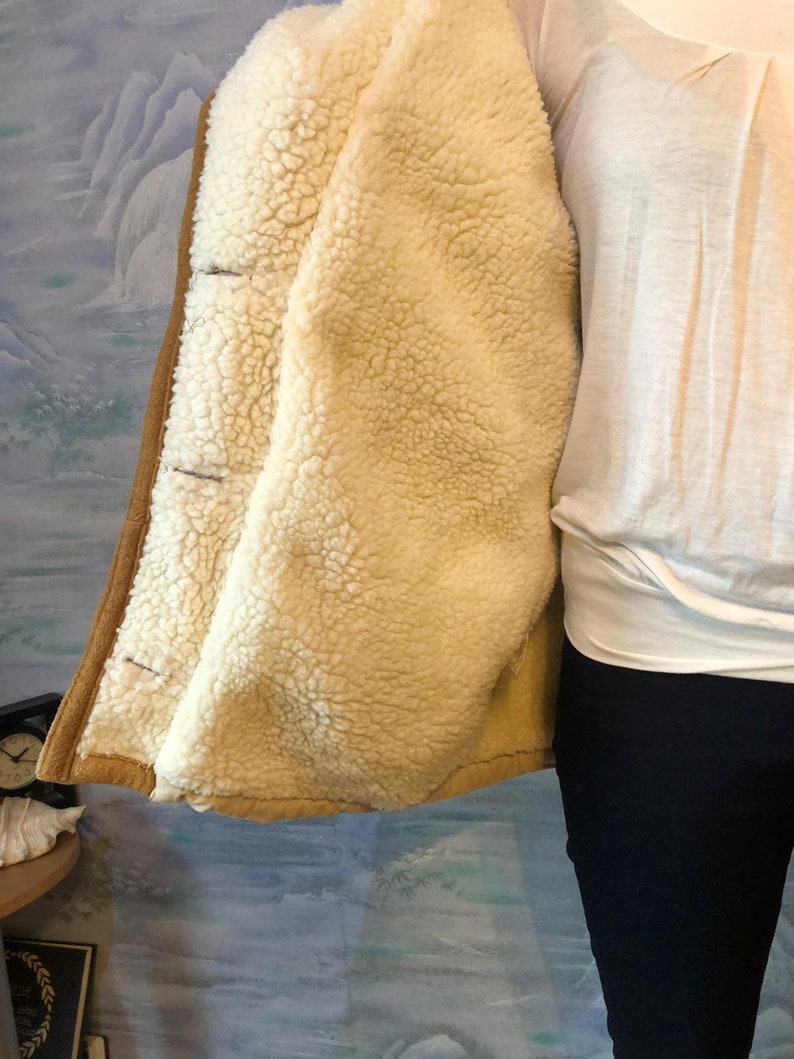 May include: A brown suede jacket with a cream-colored sherpa lining. The jacket has a button closure and a collar.
