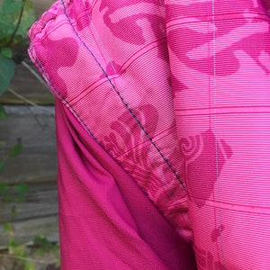 May include: Close-up of a pink fabric with a subtle pattern. The fabric has a textured, woven appearance and a slightly shiny finish.