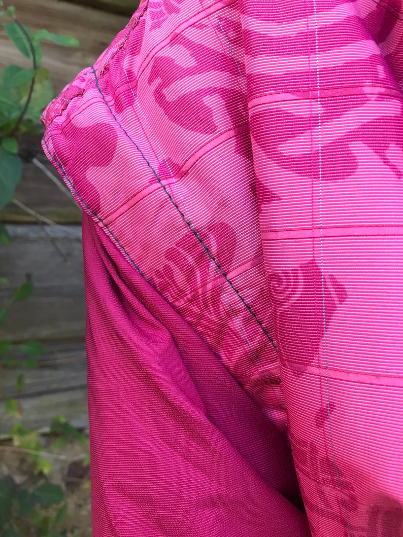 May include: Close-up of a pink fabric with a subtle pattern. The fabric has a textured, woven appearance and a slightly shiny finish.