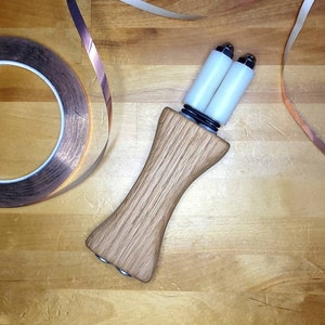 May include: A wooden tool with two white rollers and a copper tape roll. The tool is used for wrapping copper tape around objects.