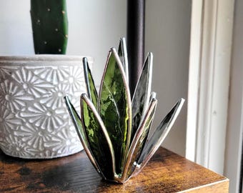 May include: A green glass succulent plant sculpture with silver accents. The sculpture is made of stained glass and is a decorative piece for a home or office.