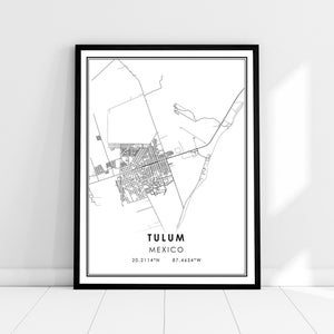 May include: A framed black and white map print of Tulum, Mexico. The map shows the city's layout with streets and surrounding areas. The text "Tulum MEXICO" and coordinates 20.2114°N 87.4654°W are printed below the map.