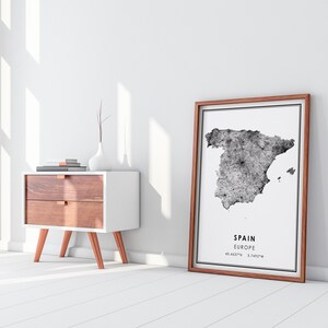 May include: A black and white print of a map of Spain with the text "SPAIN EUROPE 40.4637&deg;N 3.7492&deg;W" in a brown frame.