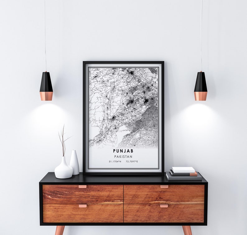 May include: Black and white map print of Punjab, Pakistan, with the coordinates 31.1764&deg;N 72.0597&deg;E. The print is framed in a black frame and hanging on a white wall above a wooden dresser with black drawer fronts.