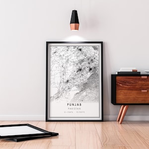 May include: Black and white map print of Punjab, Pakistan, with the text "PUNJAB PAKISTAN 31.1704&deg;N 72.7097&deg;E" in the bottom right corner. The print is framed in a black frame and is hanging on a white wall.
