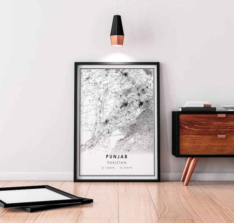 May include: Black and white map print of Punjab, Pakistan, with the text "PUNJAB PAKISTAN 31.1704&deg;N 72.7097&deg;E" in the bottom right corner. The print is framed in a black frame and is hanging on a white wall.